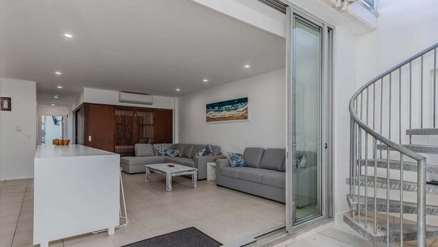 A modern living room with a sofa, coffee table, and a glass door leading to a staircase. - Coastal Luxe Rooftop Escape - Paradiso 345 (Tweed)