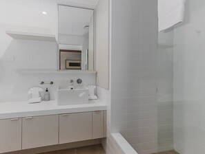 A modern bathroom with a white sink, mirror, and shower area. - Coastal Luxe Rooftop Escape - Paradiso 345 (Tweed)