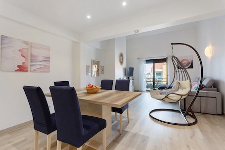 A modern dining area with a wooden table and dark chairs, a hanging chair, and a sofa in the background.. Pedra do Ouro Yoga Retreat Apartment near Beach and Pool