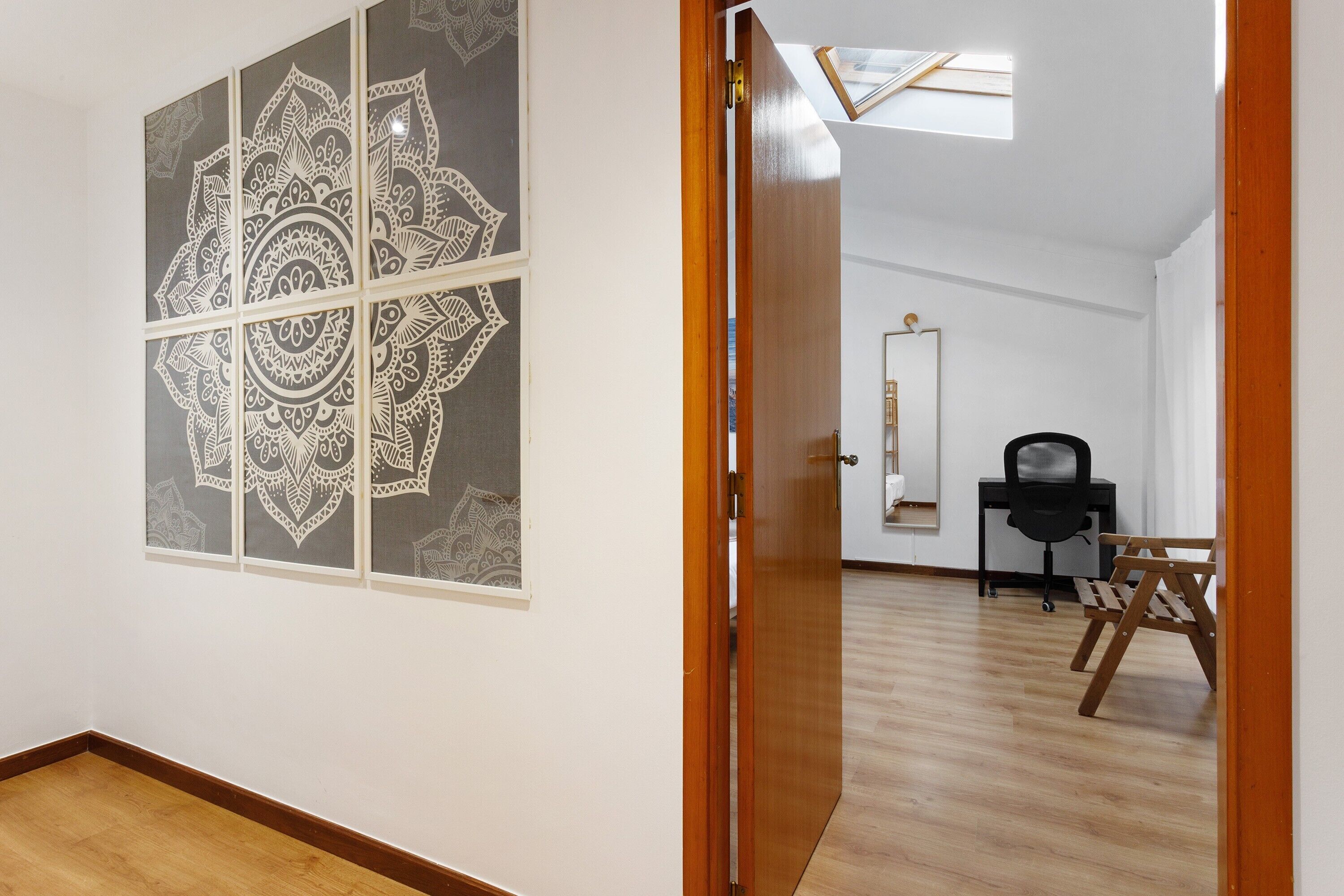 A room with a wooden floor, a door, a chair, a desk, and a wall with a geometric pattern.