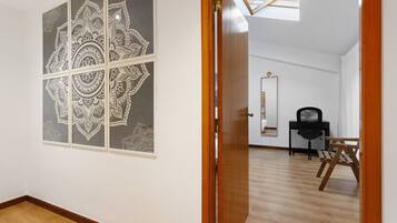 A room with a wooden floor, a door, a chair, a desk, and a wall with a geometric pattern.