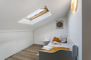 Un dormitorio con tragaluz, una cama con almohadas, una mesita de noche con una vela y una decoración en la pared.
