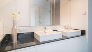 Ein modernes Badezimmer mit zwei Waschbecken, einem großen Spiegel und einer Blumenvase.