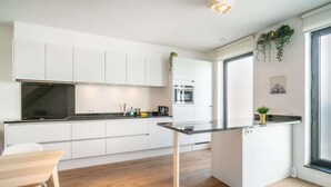 Eine moderne Küche mit weißen Schränken, einer zentralen Kochinsel und einem Fenster mit Pflanzen.