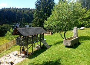 Ett lekstuga i trä med en rutschkana, en stengrunn och en inhägnad trädgård.