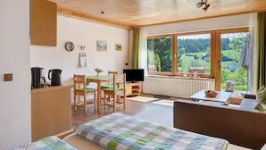 Ein Zimmer mit einem Bett, einem Schreibtisch mit Computer, einem Stuhl, einem Tisch mit Schüssel und einem Fenster mit Blick ins Grüne.