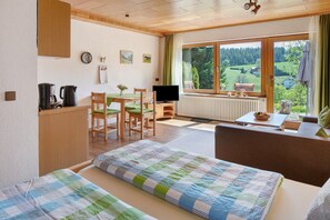 Una stanza con un letto, una scrivania con un computer, una sedia, un tavolo con una ciotola e una finestra vista sul verde.