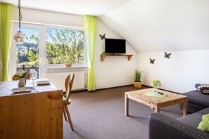Una sala de estar con comedor, un televisor montado en la pared y vistas a zonas verdes.