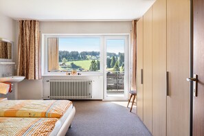 A bedroom with a bed, a window with a view of a green landscape, a radiator, and a wooden wardrobe. - Bright Feldberg Apartment on Farm with Private Balcony and Green Views (Schönwald im Schwarzwald)