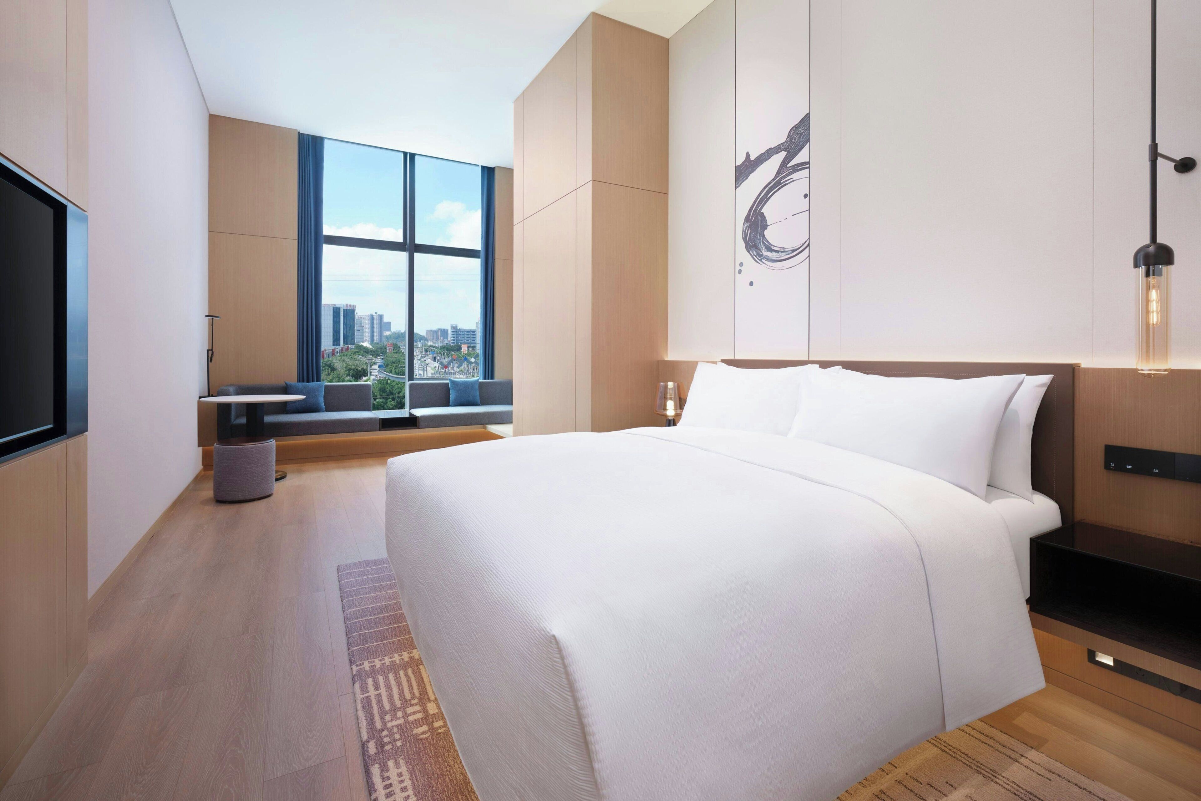 Una habitación de hotel moderna con una cama grande, un televisor, una ventana con vista a la ciudad y una obra de arte colgada en la pared.