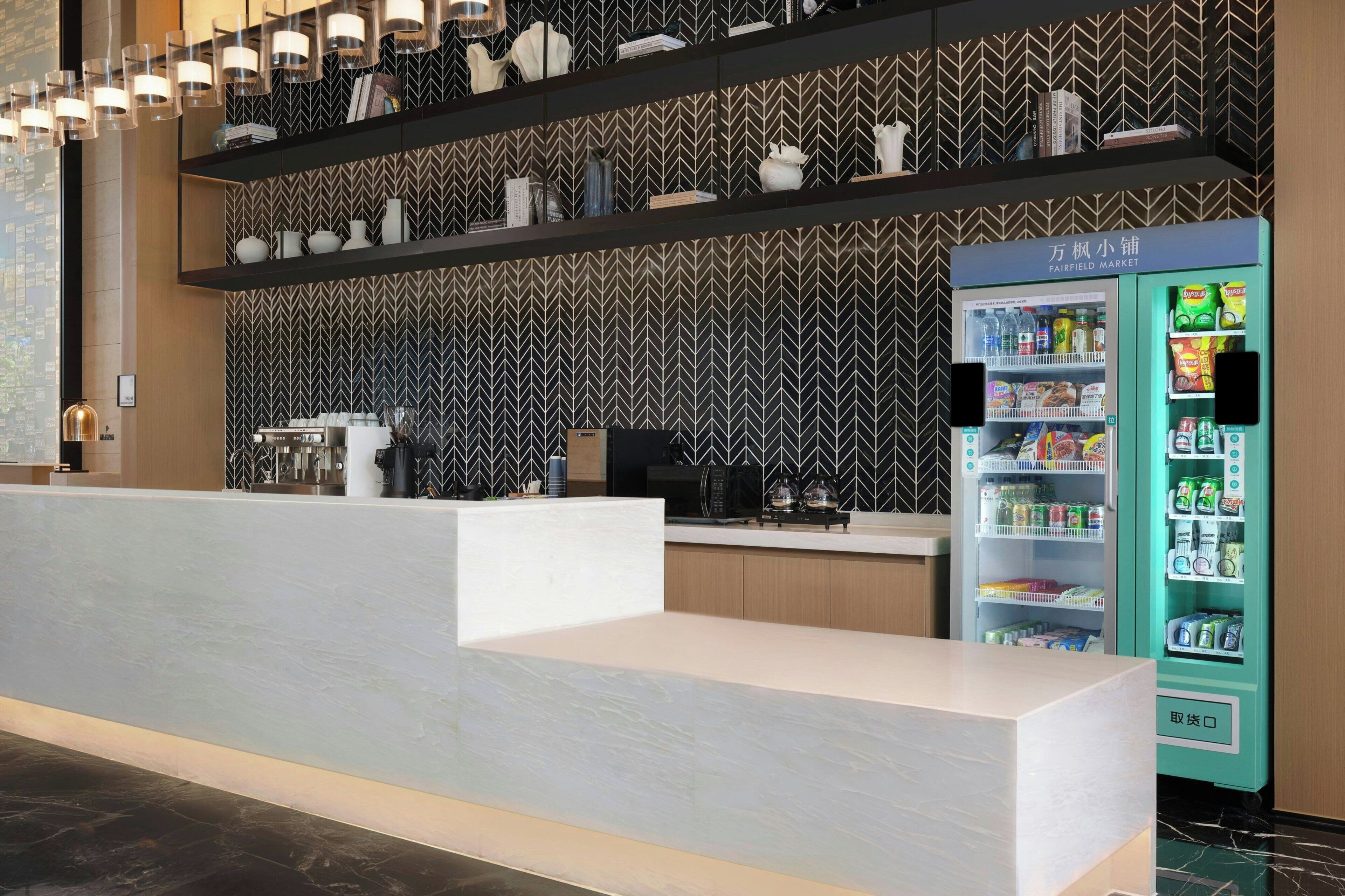Un espace d’accueil moderne avec un comptoir de réception blanc, un distributeur automatique et un mur décoré de motifs.