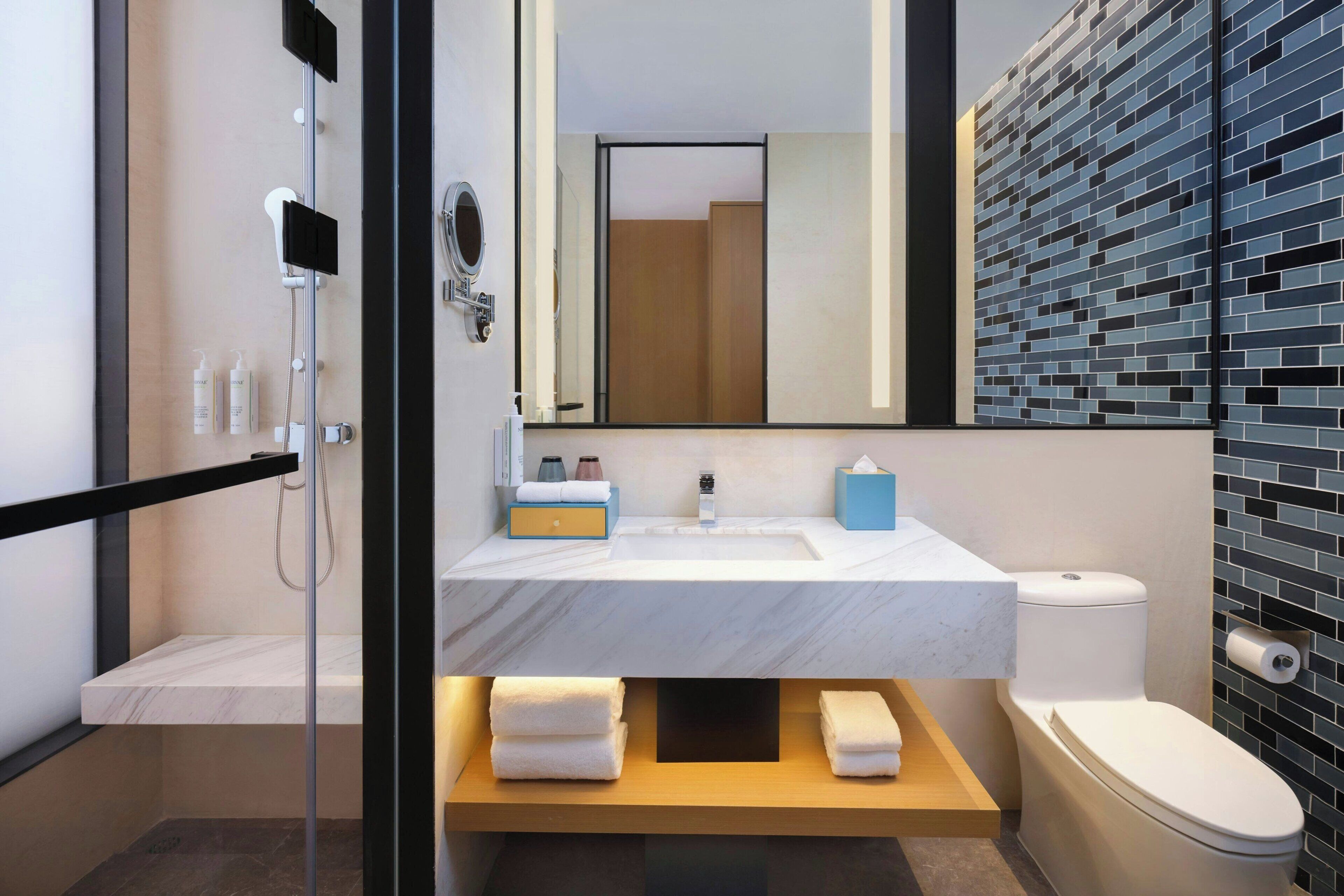 A modern bathroom with a glass shower enclosure, a marble sink, a toilet, and a wooden vanity.