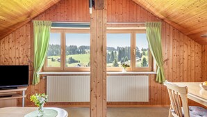 Una habitación con paneles de madera, una ventana grande, una mesa con un jarrón de flores, una silla y un televisor.