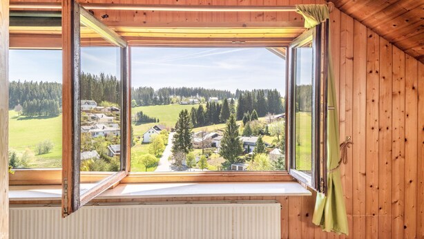 Una habitación con un ventanal que ofrece vistas a un paisaje rural con casas y árboles.