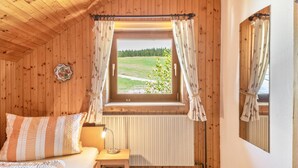 Una habitación con paneles de madera, una cama, una mesita con lámpara, una ventana con cortinas y un radiador.