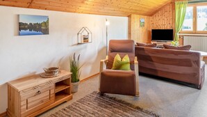 Una habitación con paneles de madera, un sofá, una silla, un televisor y una ventana con cortinas.