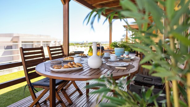 A wooden deck with a round table set for breakfast, surrounded by chairs, with a view of buildings in the background. - Fiore D’oriente Apartment 2, Apartment (Rhodes)