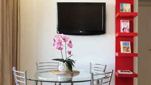 A dining area with a glass table, metal chairs, a potted orchid, a red bookshelf, and a mounted TV. - Fiore D’oriente Apartment 2, Apartment (Rhodes)
