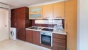 A compact kitchen with wooden cabinets, a built-in oven, a washing machine, and a coffee maker. - Fiore D’oriente Apartment 2, Apartment (Rhodes)
