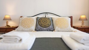 A neatly made bed with three pillows, two bedside tables with lamps, and a folded towel on the floor. - Fiore D’oriente Apartment 2, Apartment (Rhodes)