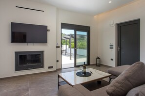 A modern living room with a flat-screen TV, fireplace, and a glass door leading to an outdoor area. - Escape to Casadi Fileri Villa, a brand-new property in the area of Ialysos. (Rhodes)