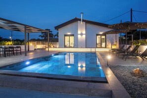 Una casa moderna amb piscina, mobiliari exterior i una zona de porxo coberta.