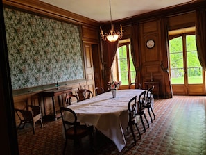 A dining room with a round table, chairs, a chandelier, and a view through large windows. - Château 'De Barral - Private Pool', Private Garden and Wi-Fi (Hauterives)