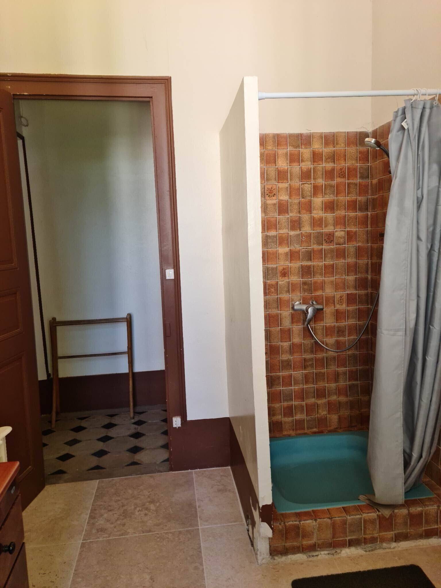 Un baño con ducha, piso de baldosas y una puerta que da a otra habitación.