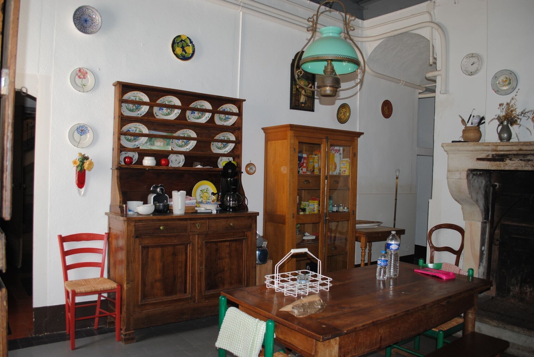 A dining room with a wooden table, chairs, a cabinet with dishes, a hanging light fixture, and a fireplace.