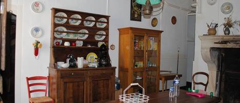 A dining room with a wooden table, chairs, a cabinet with dishes, a hanging light fixture, and a fireplace.