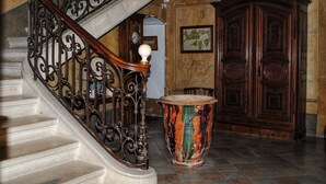 Una imponente escalera con barandillas de metal ornamentadas, una puerta de madera y un gran jarro decorativo.