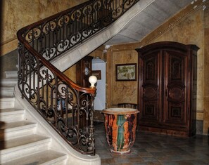 A grand staircase with ornate metal railings, a wooden door, and a large decorative urn.