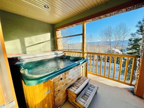 Uma cabana de madeira com hidromassagem, um banco de madeira e uma varanda com vista para árvores e montanhas cobertas de neve.