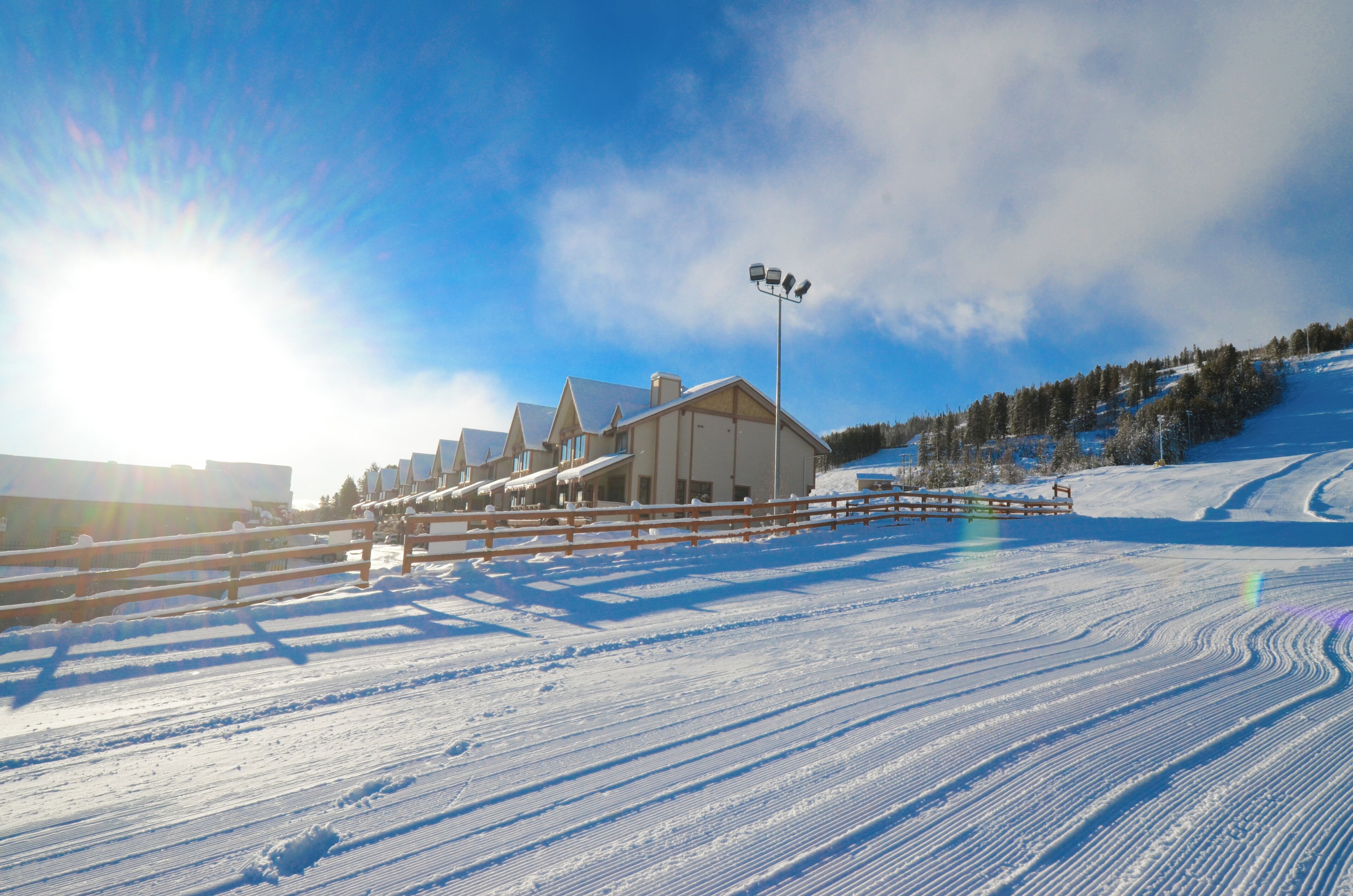 Estación de esquí cubierta de nieve con una cabaña, una valla de madera y cielo despejado.