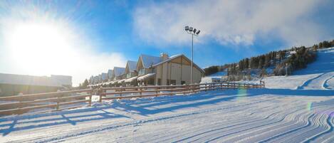 Estación de esquí cubierta de nieve con una cabaña, una valla de madera y cielo despejado.