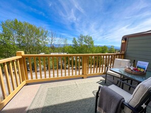 Um deck com guarda-corpo de madeira, uma mesa com cadeiras, uma cesta de frutas e um guia do hotel sobre a mesa.