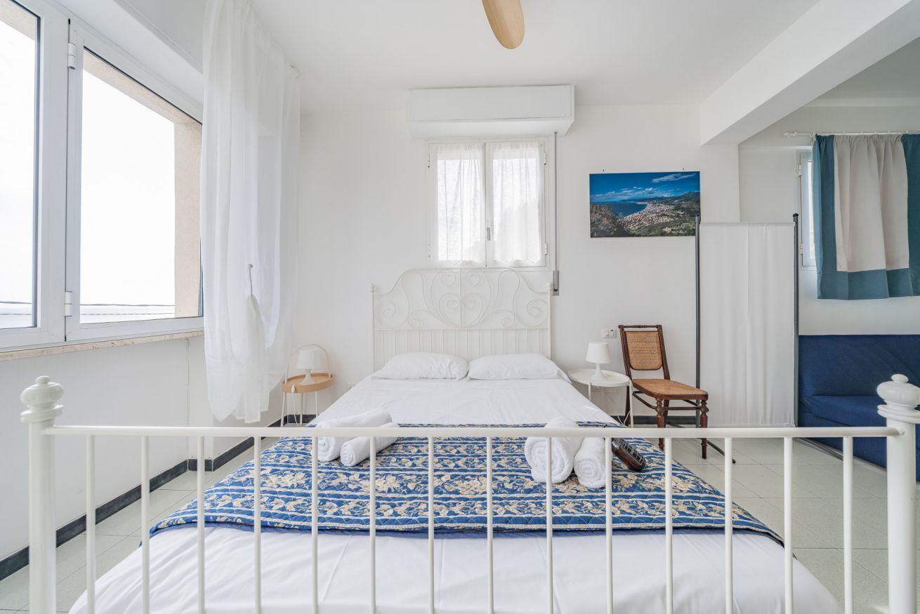 Une chambre à coucher avec un lit, une fenêtre, une chaise, une table de chevet et un tableau au mur.