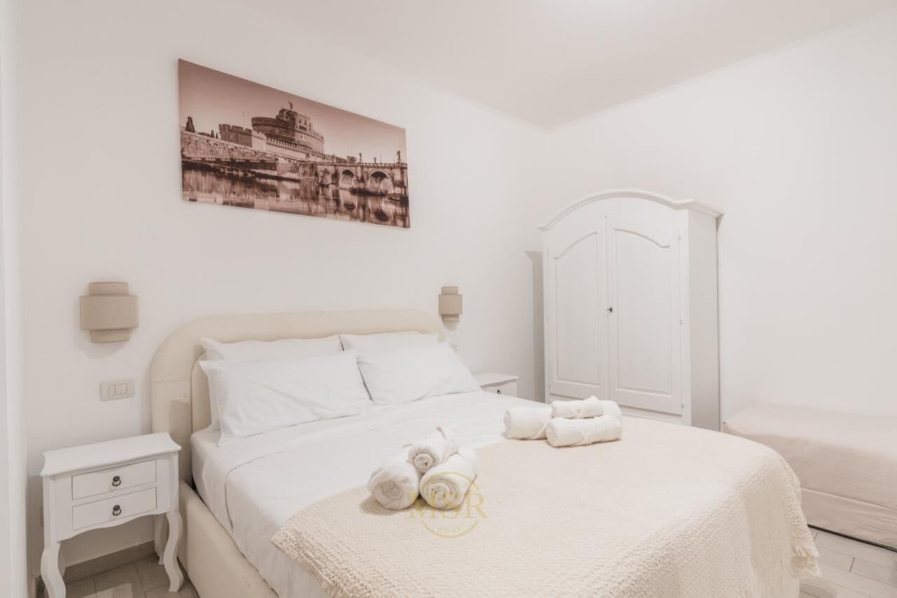 A white bedroom with a bed, a nightstand, a wardrobe, and a wall-mounted picture.