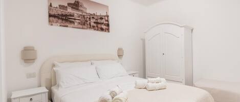 A white bedroom with a bed, a nightstand, a wardrobe, and a wall-mounted picture.