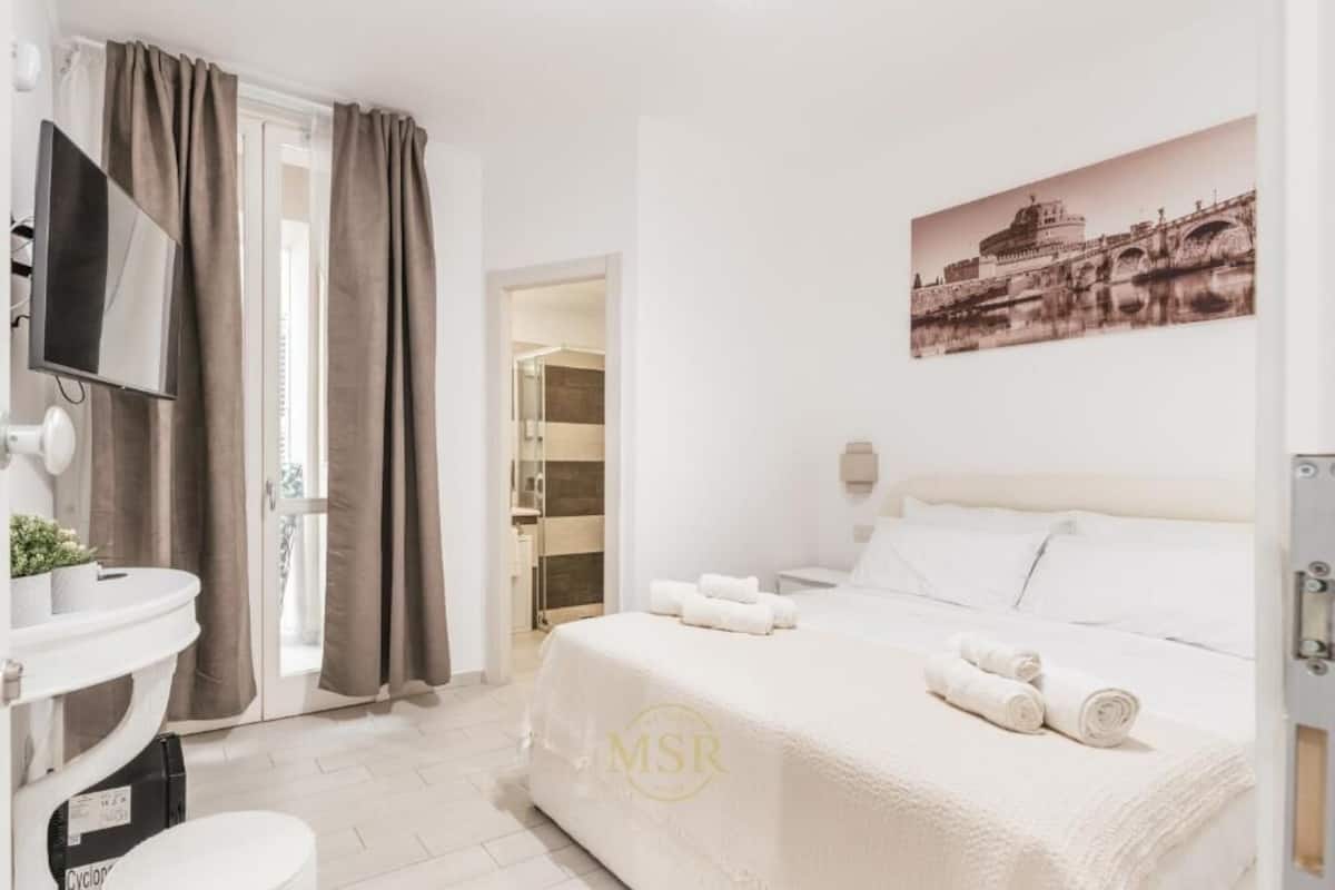 A hotel room with a bed, a TV, a bathroom with a sink, and a shower.