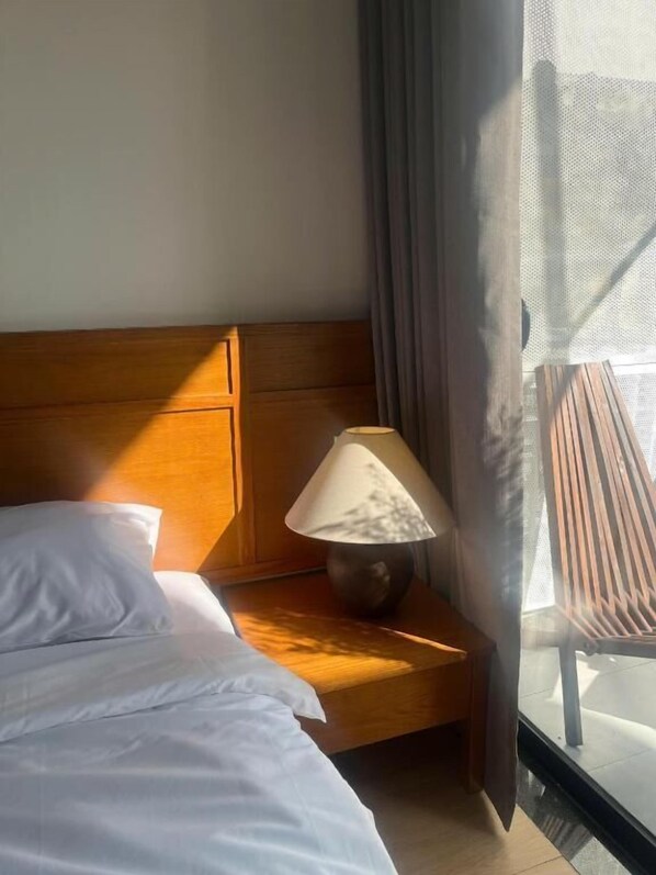 Une chambre d’hôtel avec un lit, une table de chevet avec une lampe et une vue sur l’extérieur, avec une chaise placée devant la fenêtre.