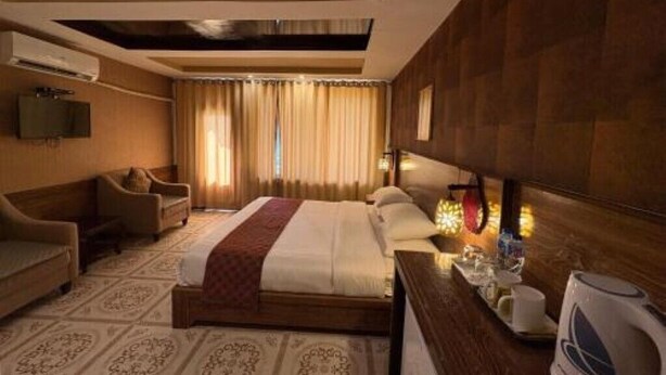 A hotel room with a bed, two armchairs, a television, a coffee maker, and a window with curtains.