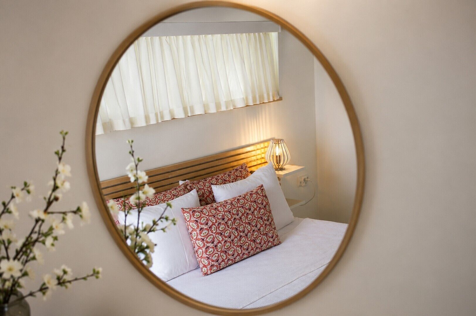 Un dormitorio con cama, almohadas, mesita de noche, lámpara y ventana con cortinas.