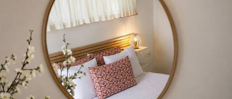 Un dormitorio con cama, almohadas, mesita de noche, lámpara y ventana con cortinas.