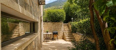 A stone-walled outdoor area with a grill, a table, and a window overlooking a mountainous landscape.
