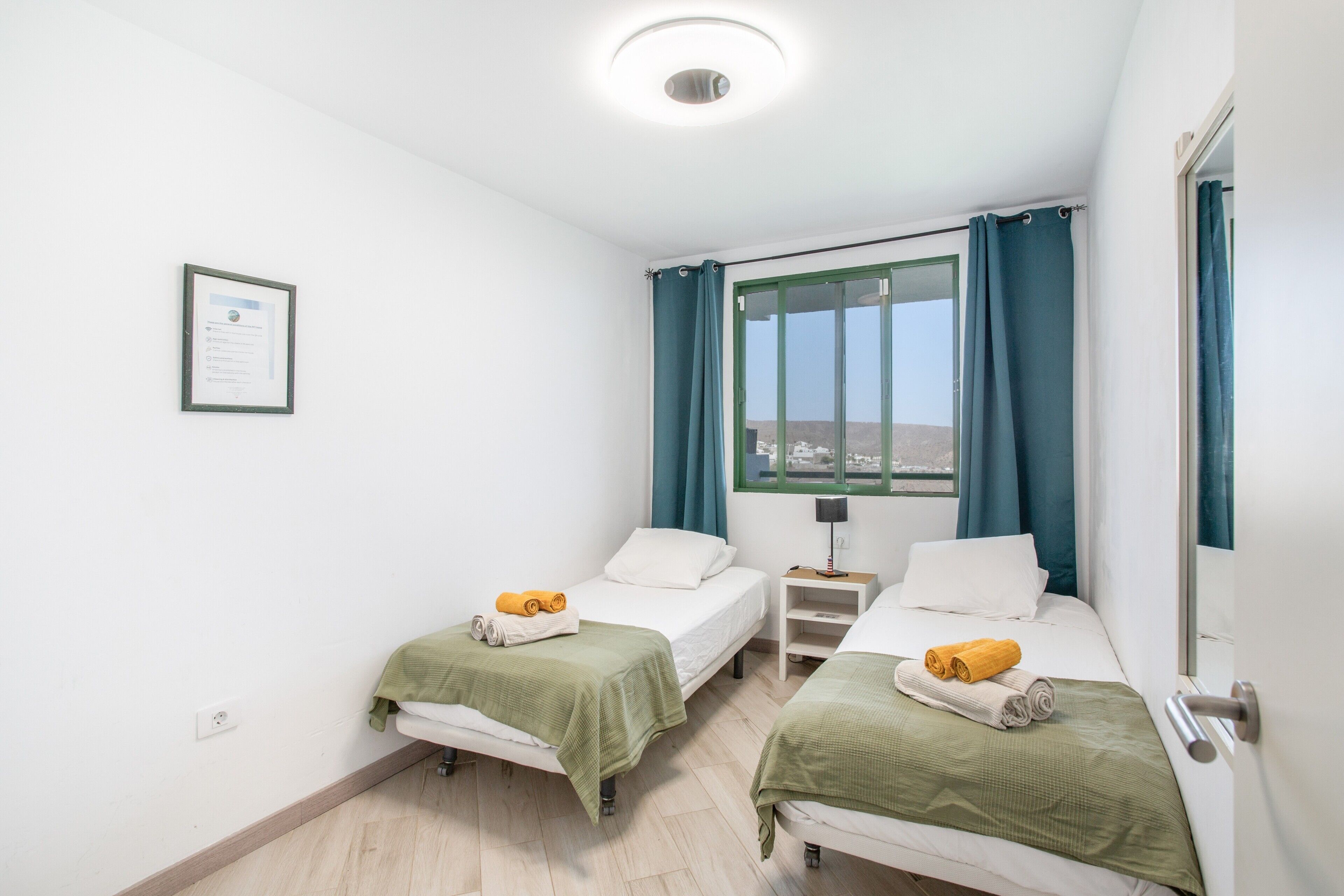 Ein Hotelzimmer mit zwei Betten, einem Nachttisch, einem Fenster mit Vorhängen und einem gerahmten Zertifikat an der Wand.