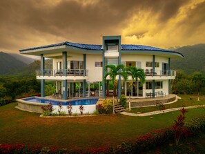 Un edificio de dos pisos con piscina, balcones y vista a las montañas.
