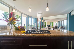 Una cocina moderna con encimera de granito, electrodomésticos de acero inoxidable y vistas al salón a través de amplios ventanales.