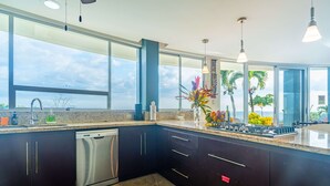 Une cuisine moderne avec des meubles de couleur sombre, un lave-vaisselle, une grande fenêtre et une vue sur le ciel.