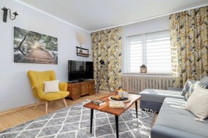 A living room with a sofa, a yellow armchair, a TV, a wooden coffee table, and a patterned wall.